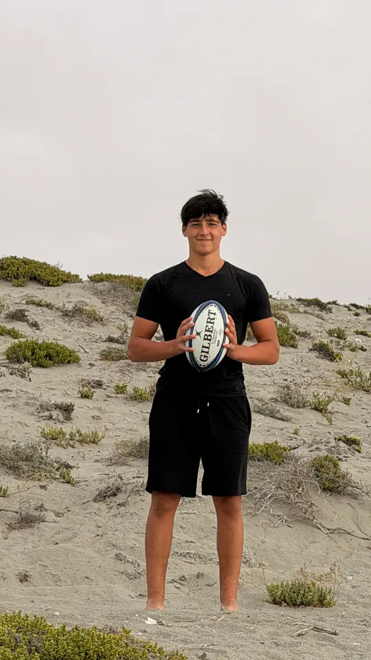 Joaquín de pie sobre las dunas sosteniendo el balón de rugby con las dos manos